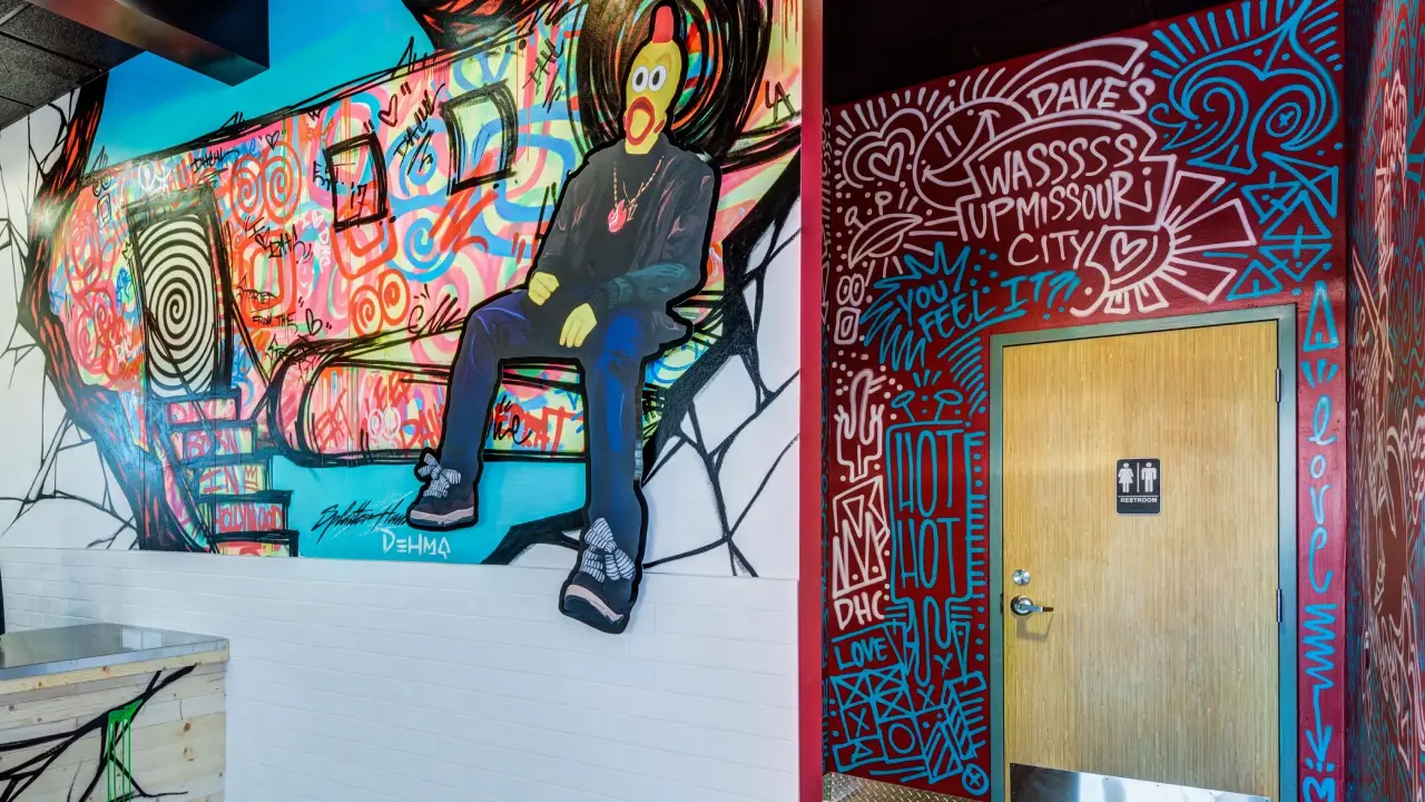 Interior of a Dave's Hot Chicken Restaurant. Accessible restroom door is shown and the iconic Dave's Hot Chicken mascot is featured in a wall mural.