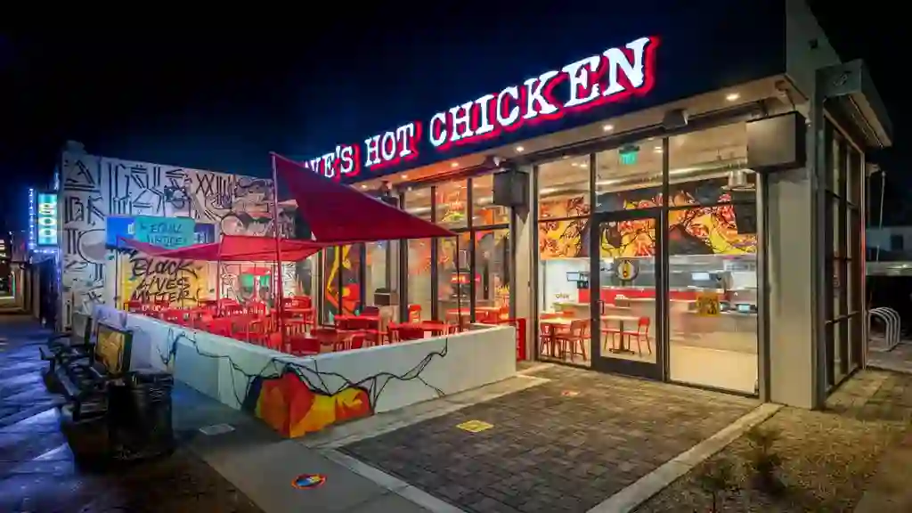 Exterior angled image of our Fried Chicken Restaurant on Fairfax in Los Angeles, CA. Pictured is the outdoor dining area with large umbrellas and a lit up sign that reads 