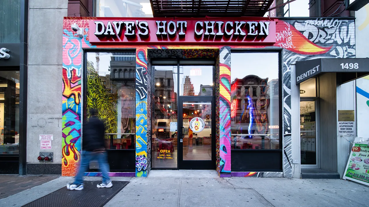 Exterior view of Dave’s Hot Chicken with vibrant graffiti and red signage on 3rd Ave, New York, NY.