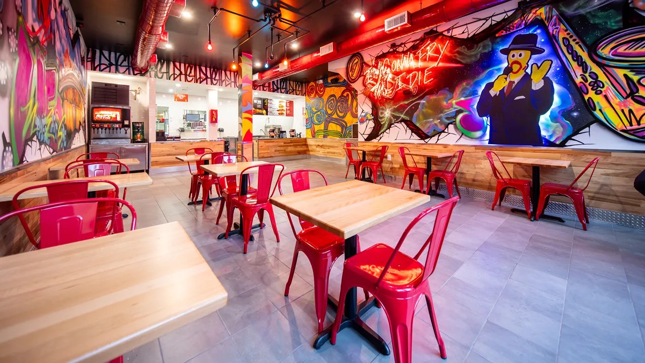 Indoor dining area featuring red chairs and colorful neon art at Dave's Hot Chicken on 3rd Ave, New York, NY.