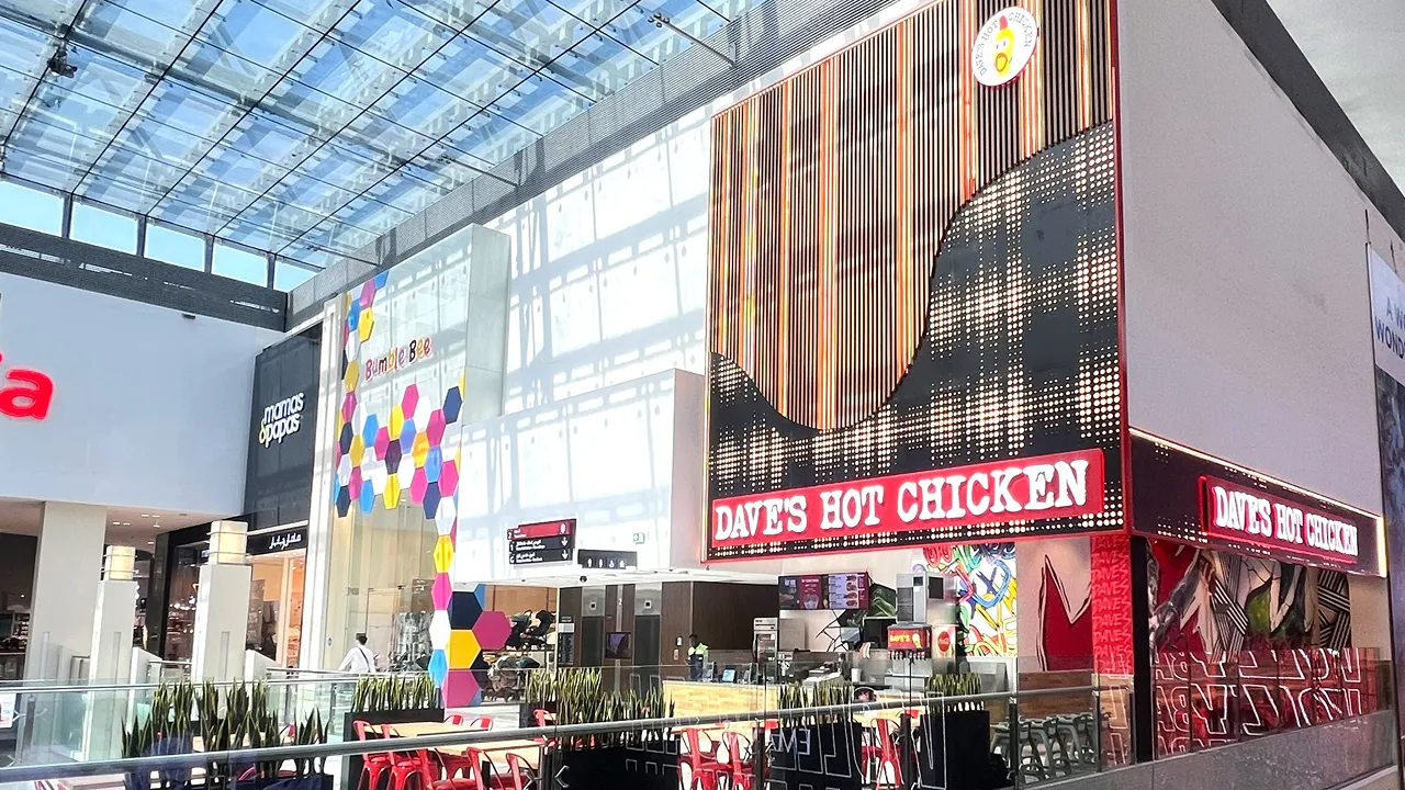 A wide view of Dave's Hot Chicken inside Dubai Mall, Dubai, showcasing the storefront with bright red chairs, signage, and the surrounding area.