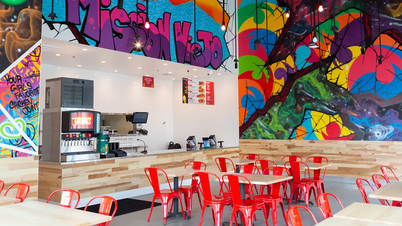 Interior view of Dave's Hot Chicken on Alicia Pkwy, Mission Viejo, CA, showcasing the dining and service area with vibrant wall art and red seating.