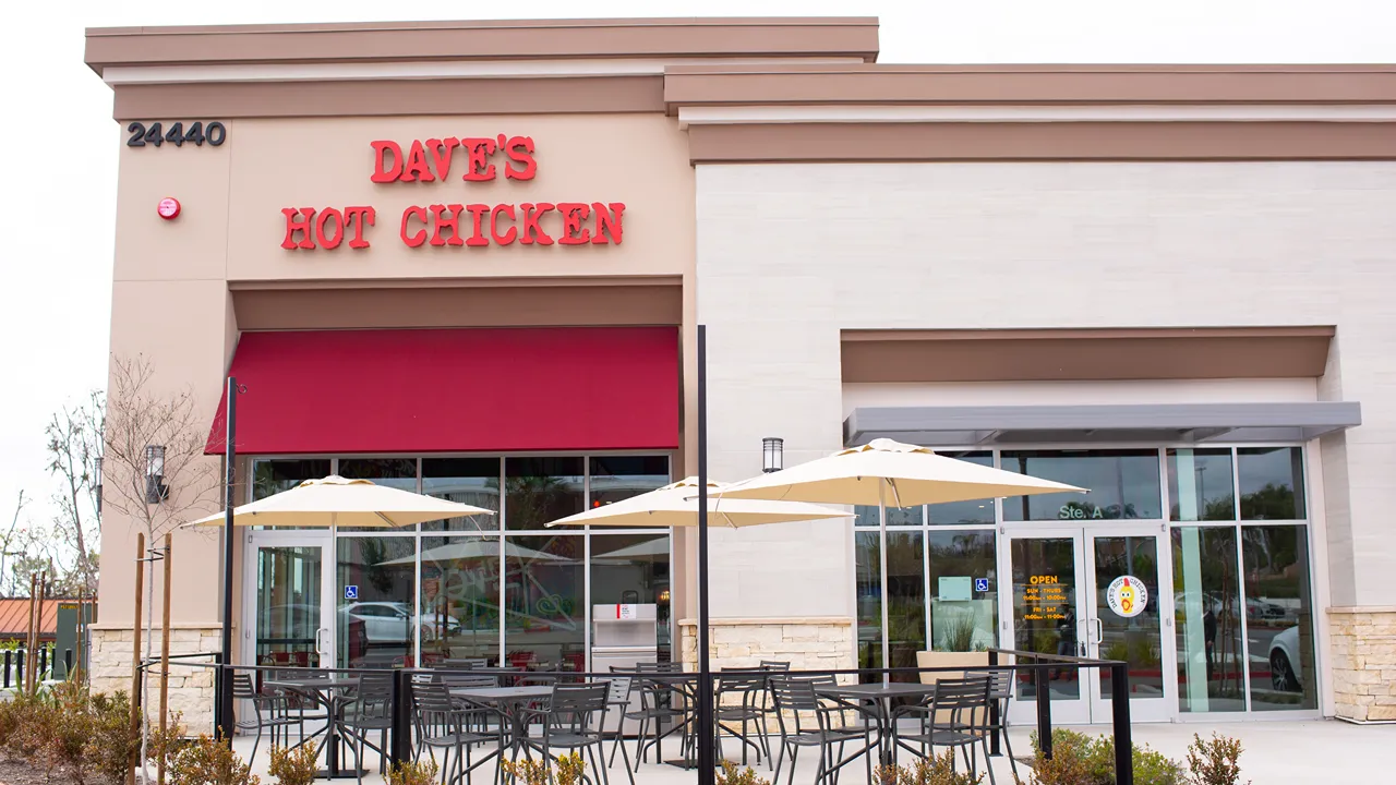 Exterior of Dave's Hot Chicken on Alicia Pkwy, Mission Viejo, CA, showing the restaurant's entrance and patio seating with umbrellas.