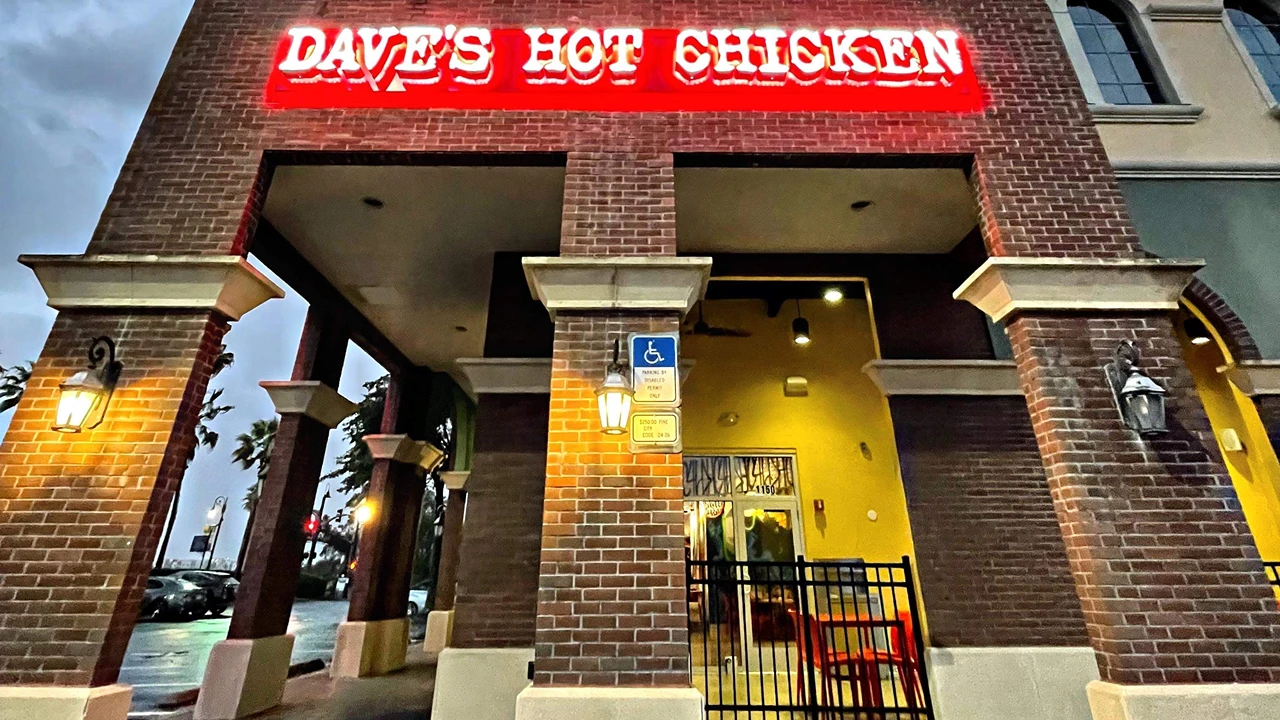 Front exterior of Dave's Hot Chicken in Altamonte Springs, FL, showing the red neon sign, brick columns, and entrance with lanterns.