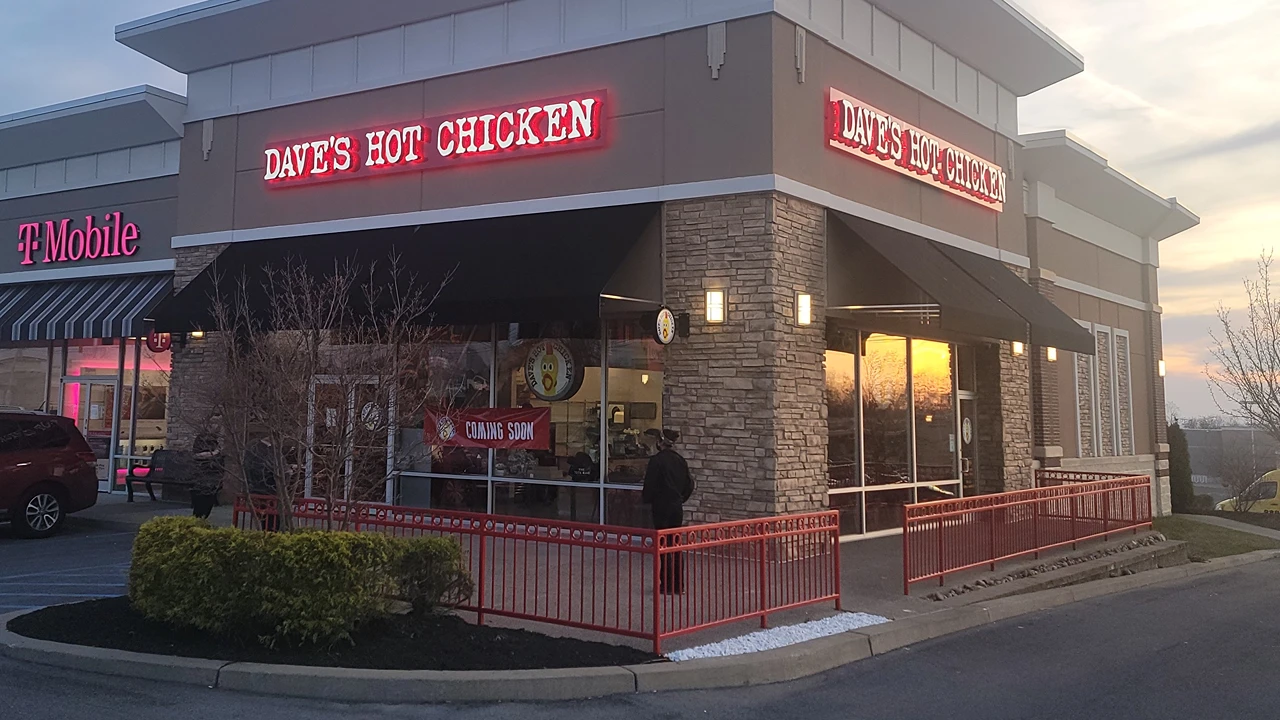 Exterior of Dave's Hot Chicken in Amsterdam, NY, with a red neon sign and storefront next to T-Mobile in a shopping plaza.