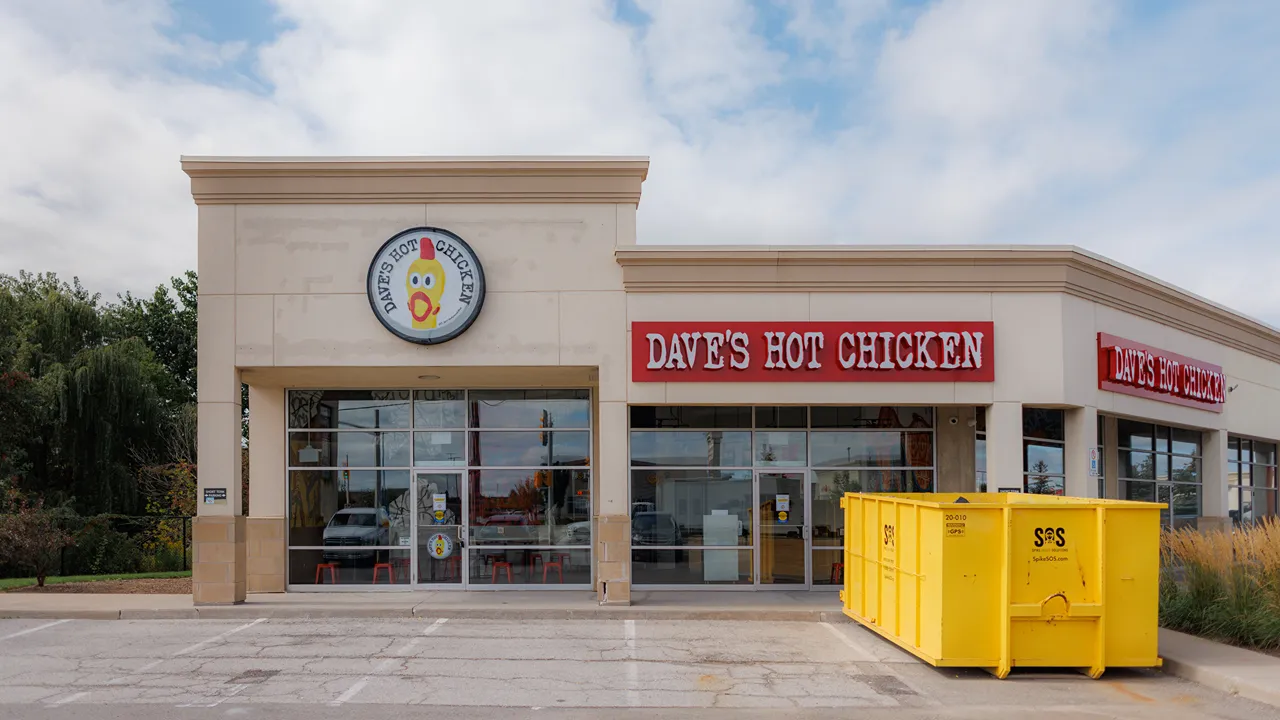 Dave's Hot Chicken storefront on Appleby Line, Burlington, ON, with a visible yellow dumpster in the parking lot.