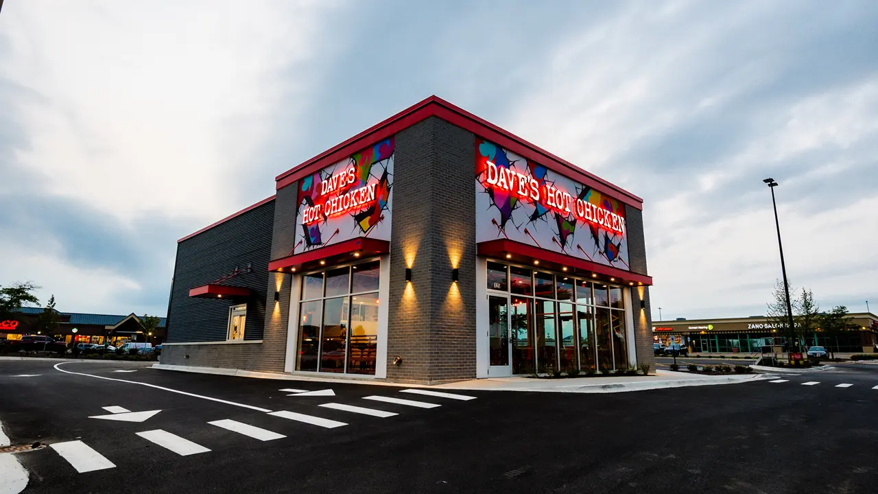 Exterior of Dave's Hot Chicken in Batavia, IL, with mural designs and large windows.