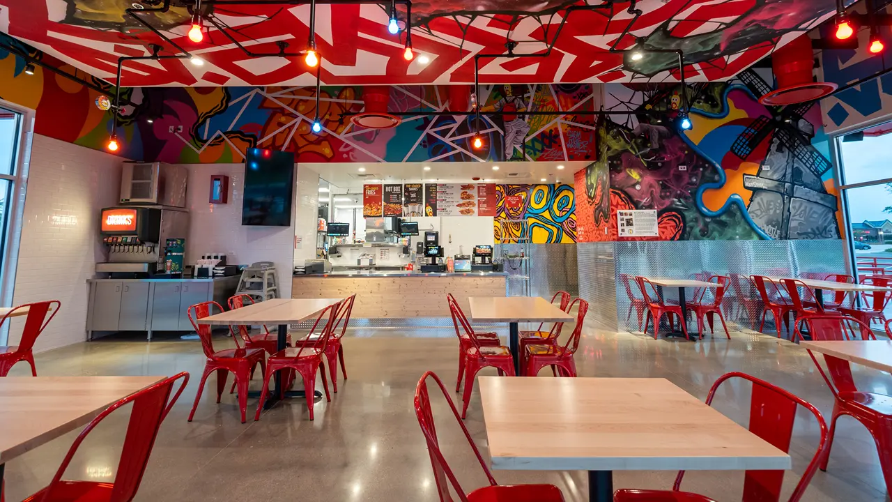 Seating area inside Dave's Hot Chicken in Batavia, IL, showcasing colorful artwork and bright red chairs.