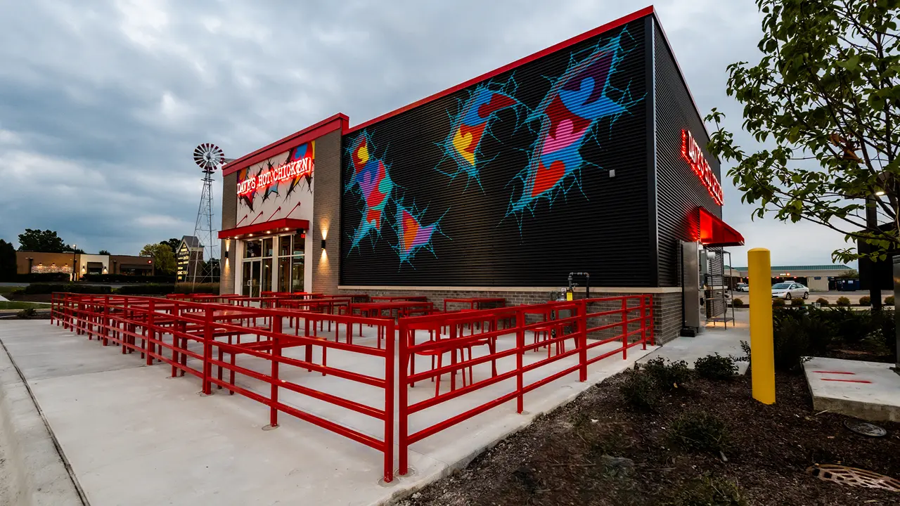 Exterior of Dave's Hot Chicken in Batavia, IL, featuring colorful murals and a red outdoor seating area.