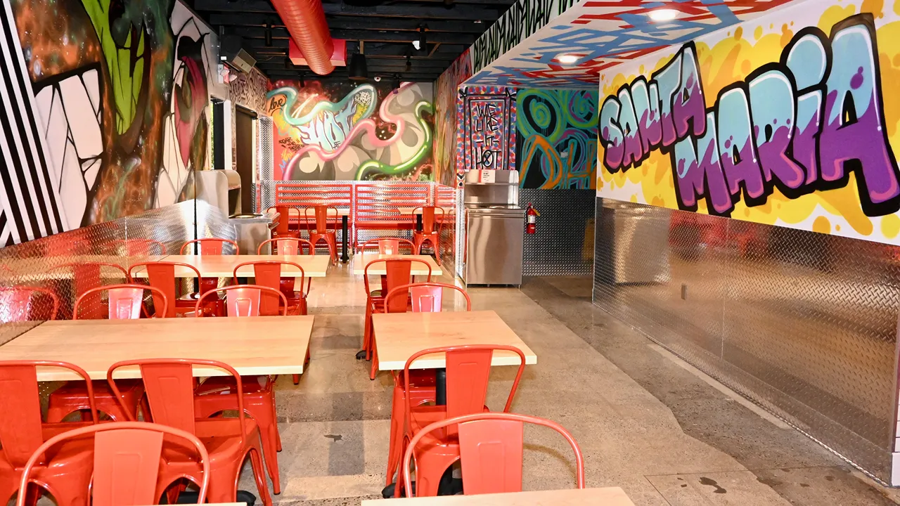 Interior dining area with red chairs, wooden tables, and colorful graffiti art on the walls at Dave’s Hot Chicken on Betteravia Rd, Santa Maria, CA.