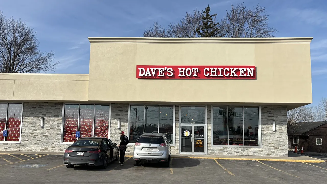 Dave's Hot Chicken Cicero, NY showing the outside of, what appears to be a new restaurant, with signage and a parking area with two parked cars.