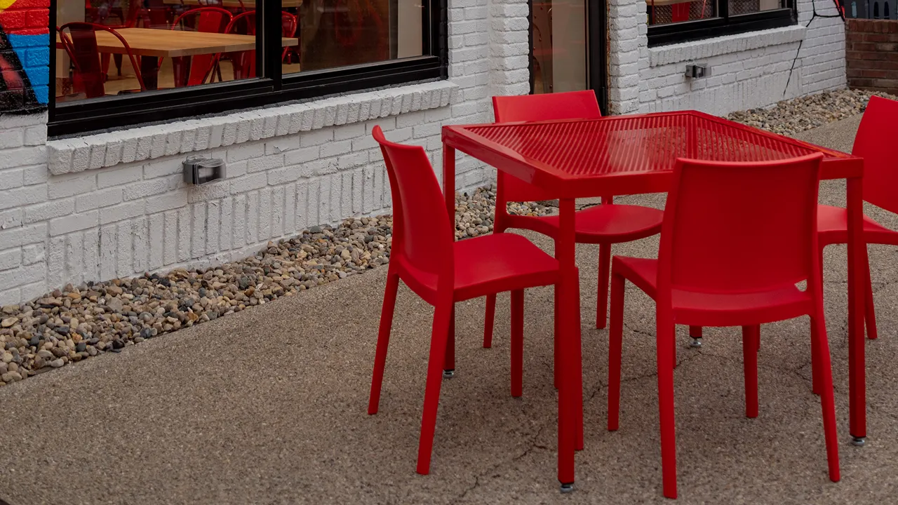 Exterior seating area at Dave's Hot Chicken on Broad Ripple Ave, Indianapolis, with red tables and chairs.