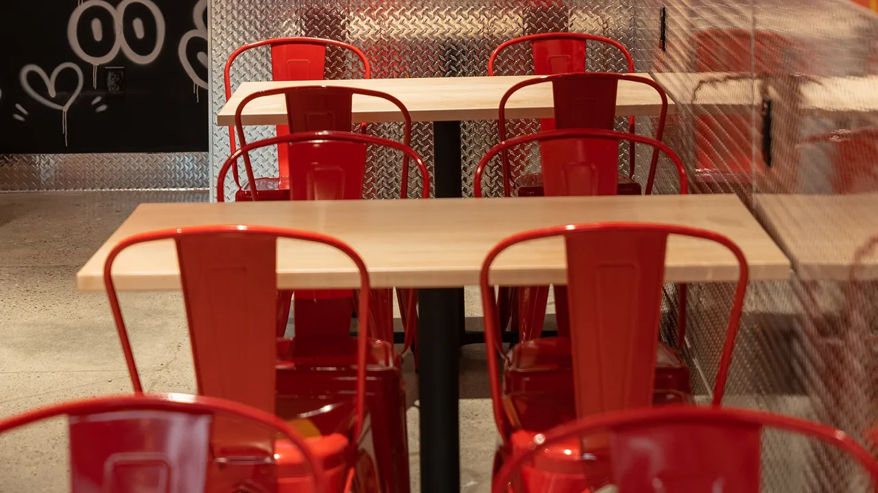 Close-up of interior seating at Dave's Hot Chicken, Broad Ripple Ave, Indianapolis, with red chairs and light wood tables.