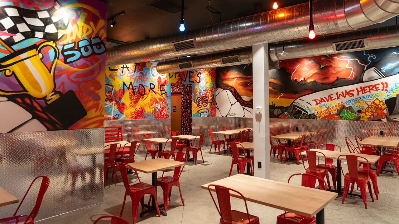 Interior view of Dave's Hot Chicken on Broad Ripple Ave, Indianapolis, featuring colorful murals and red seating.