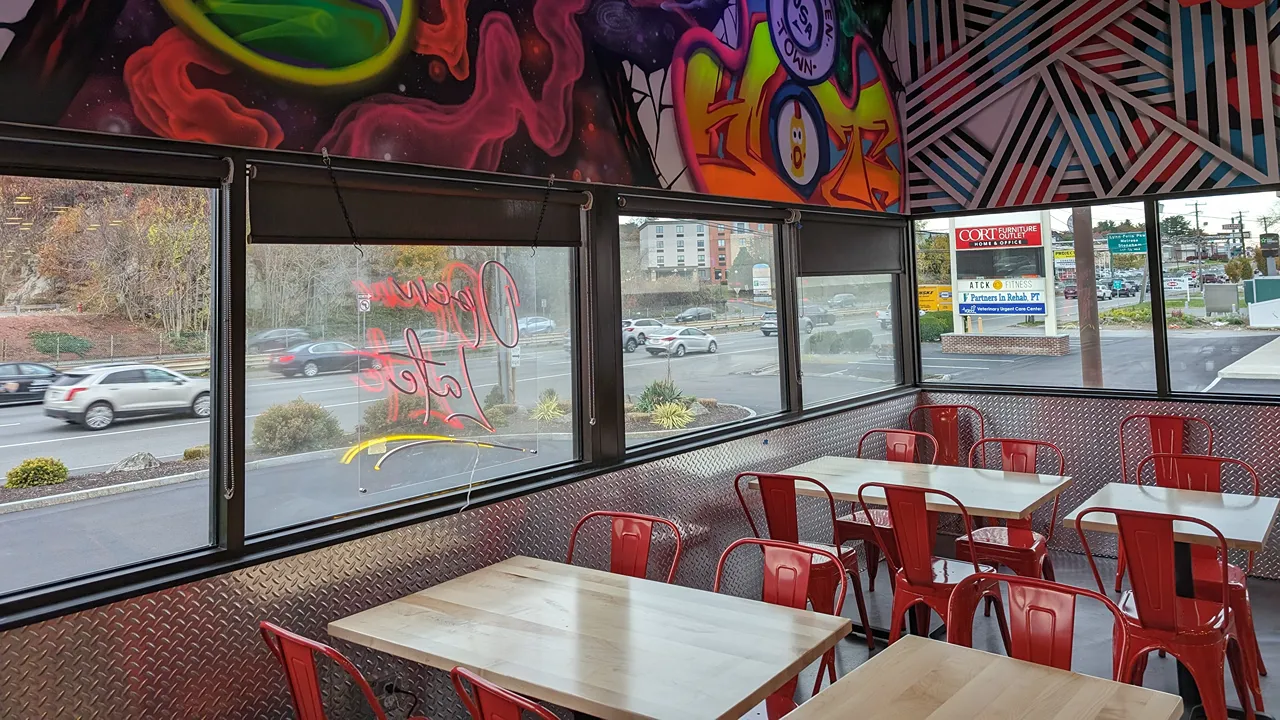 Close-up of dining area with red chairs and vibrant wall art near the windows at Dave’s Hot Chicken on Broadway, Saugus, MA.