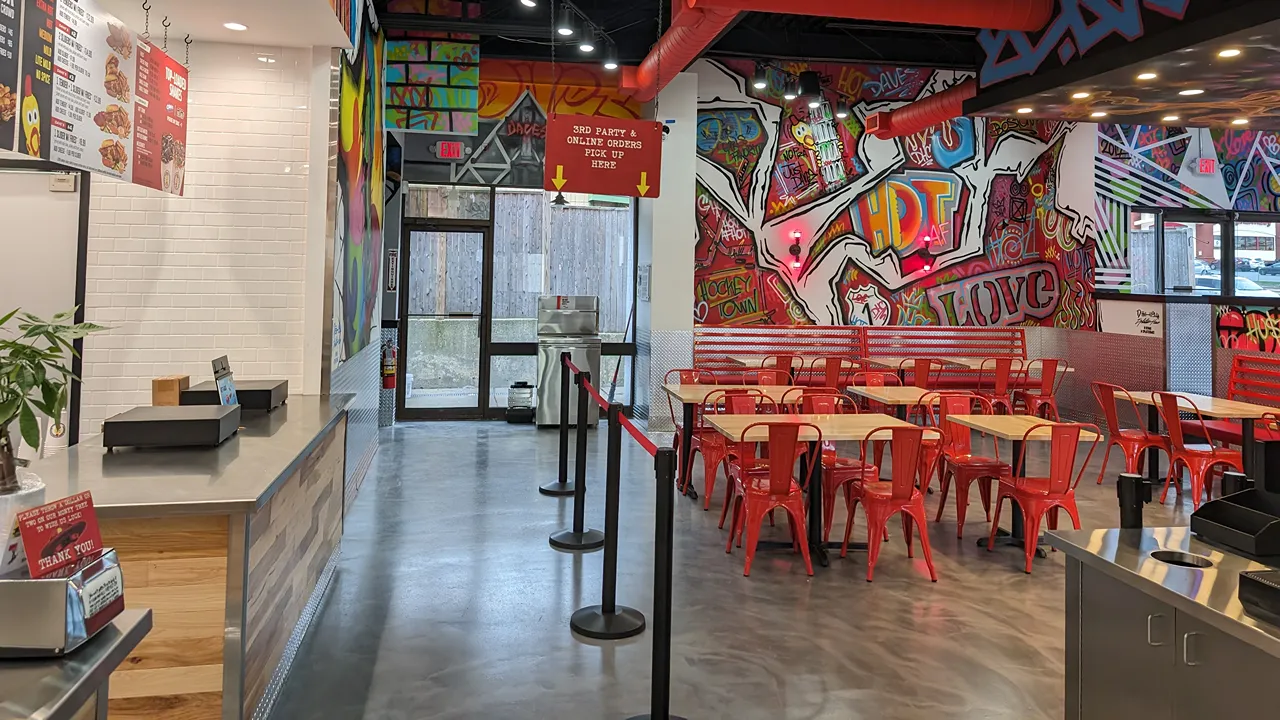 Dining area with red chairs near the entrance, showcasing street traffic through the windows at Dave’s Hot Chicken in Saugus, MA.