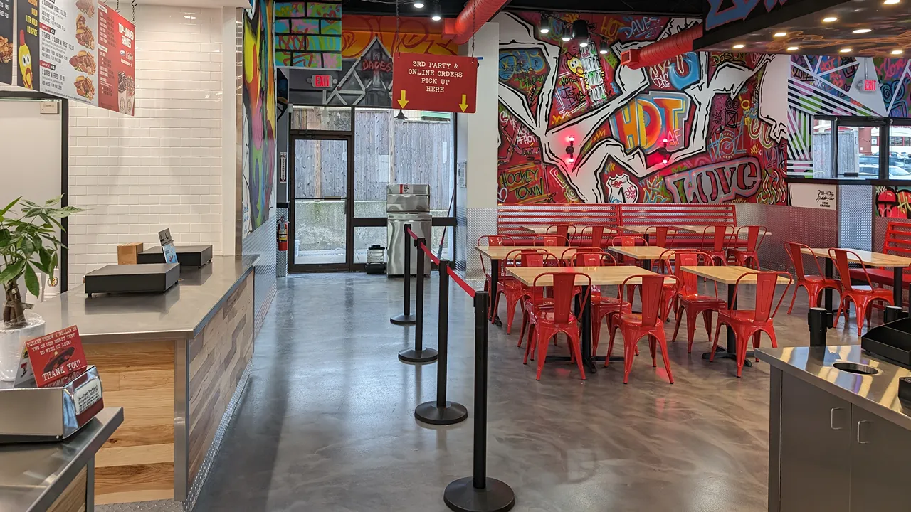 Interior dining area with tables, red chairs, and colorful wall art at Dave’s Hot Chicken on Broadway in Saugus, MA.