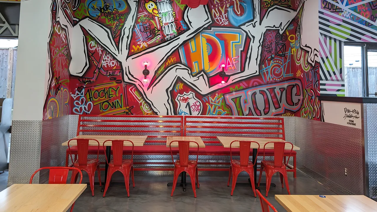 Wall art with 'Hockey Town' text and red seating in the dining area at Dave’s Hot Chicken, Broadway, Saugus, MA.