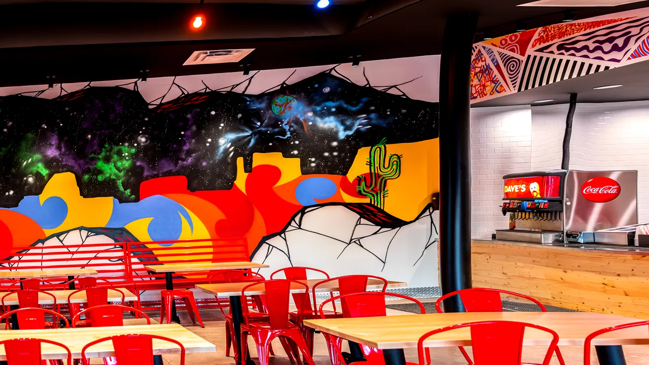 Red chairs and tables with artistic wall murals at Dave’s Hot Chicken in City View Center, Fort Worth, TX.