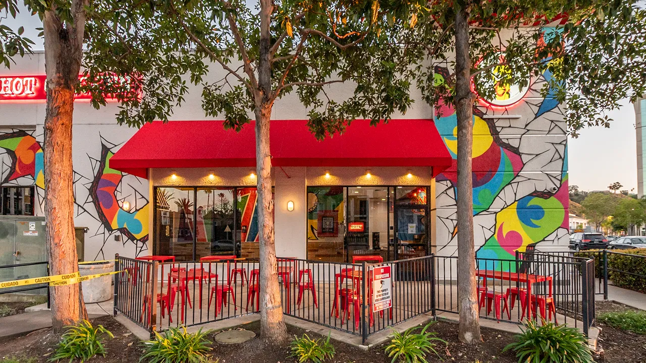 Exterior view of Dave's Hot Chicken with red awning, patio seating, and vibrant mural at Camino De La Reina – Mission Valley, San Diego, CA.