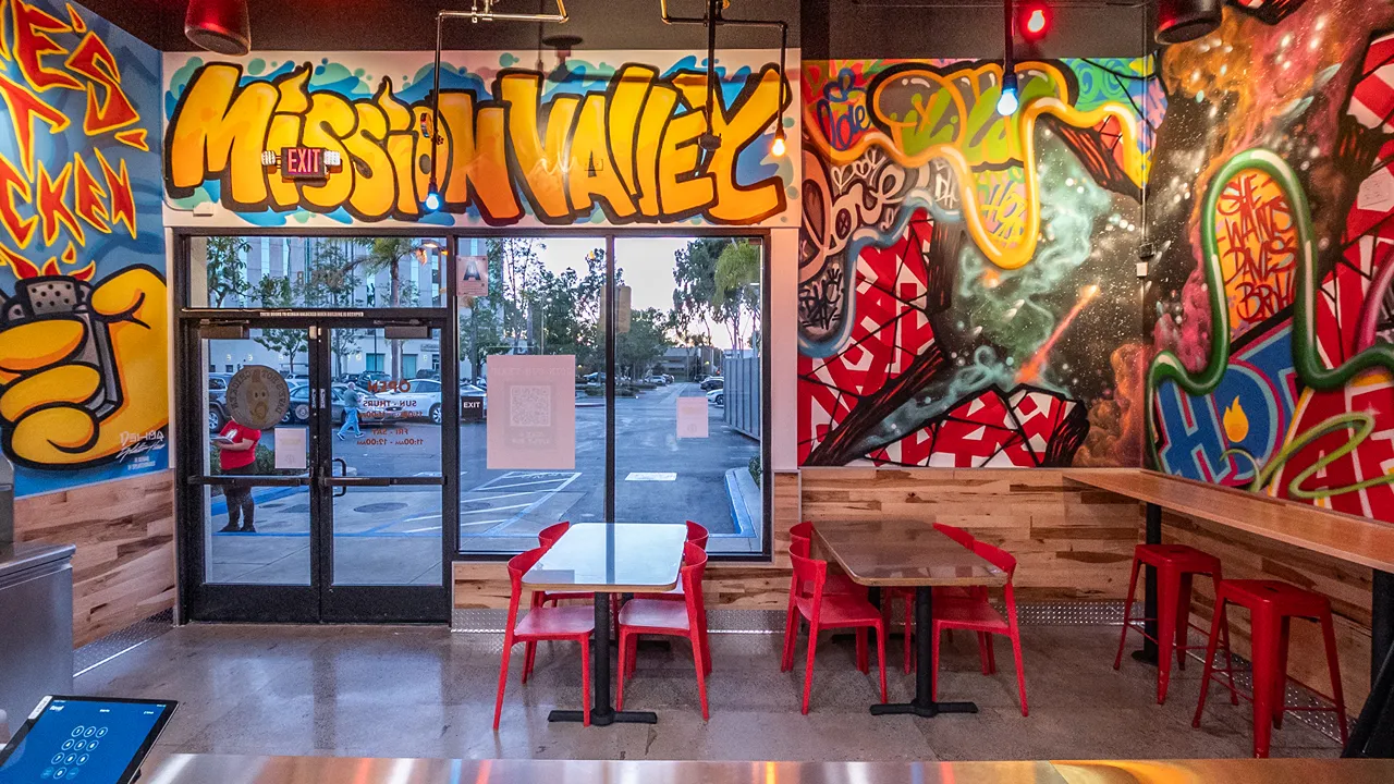 Interior dining area with red chairs and tables, graffiti art on the walls, and vibrant natural light at Dave's Hot Chicken, Camino De La Reina – Mission Valley, San Diego, CA.