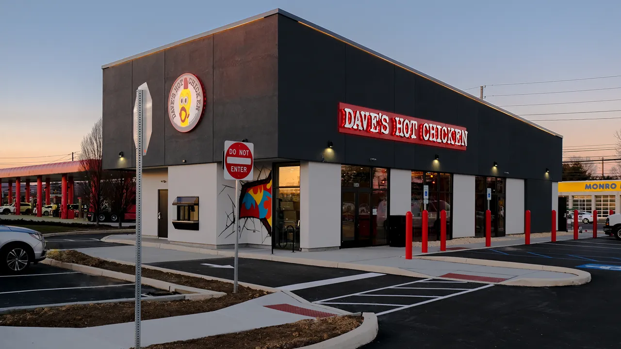 Angled view of Dave's Hot Chicken on Carlisle Pike, Mechanicsburg, PA, with a Drive-through, parking lot and bright red signage at sunset.