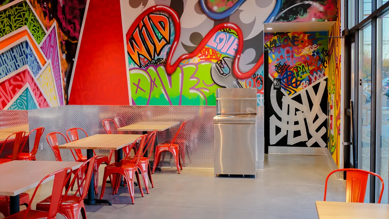 Interior seating area at Dave's Hot Chicken on Carlisle Pike, Mechanicsburg, PA, showcasing vibrant murals and red chairs.