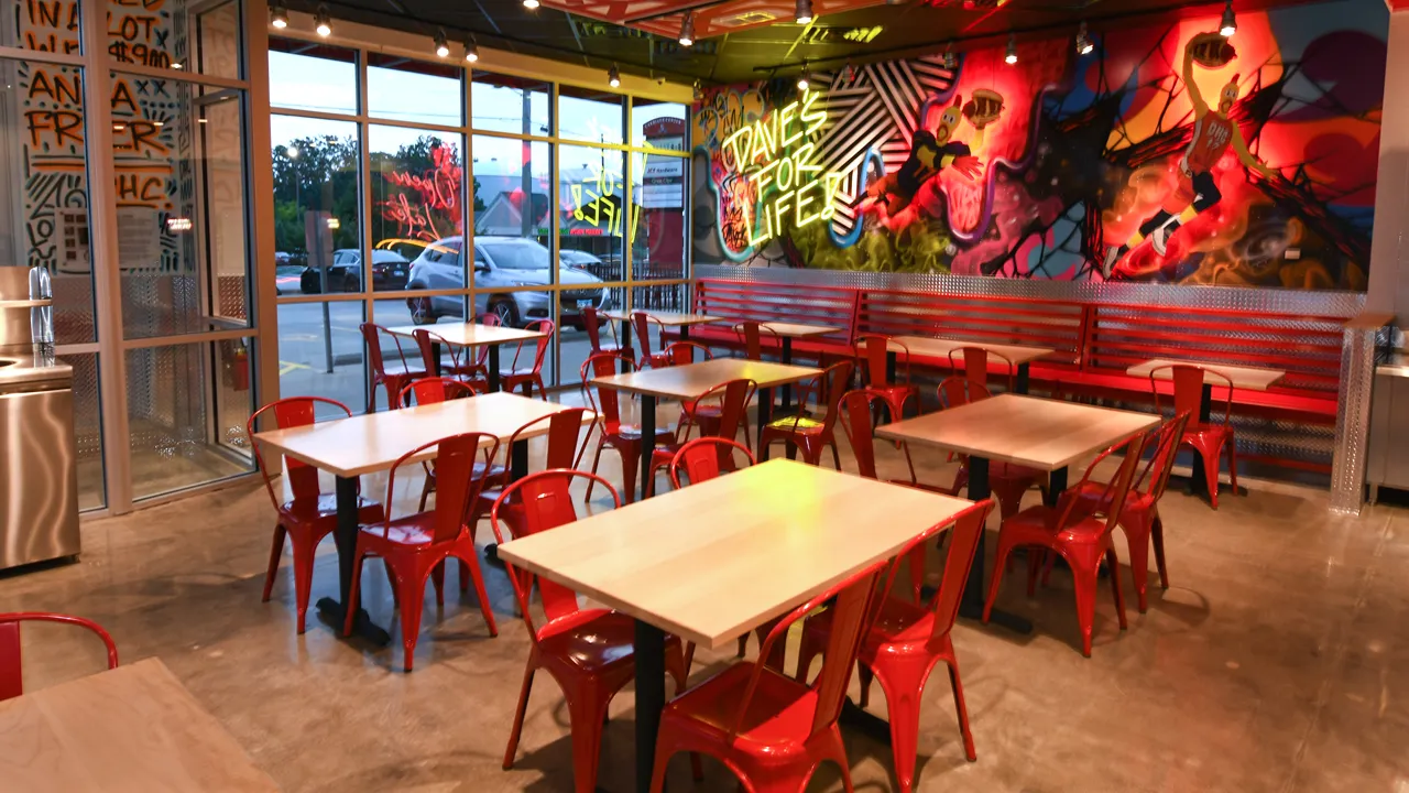 Interior shot of Dave's Hot Chicken, Champaign, IL, featuring red seating and colourful mural art.