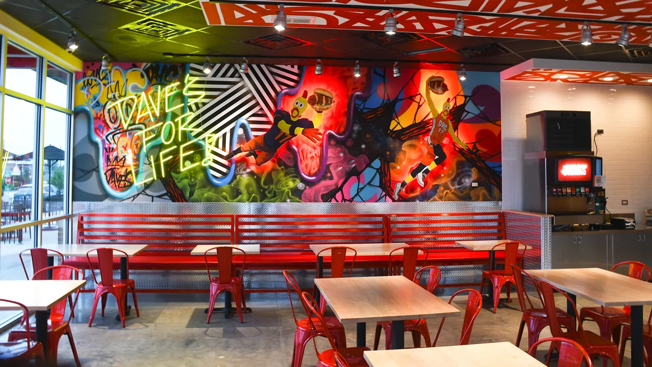 Interior view of Dave's Hot Chicken, Champaign, IL, showcasing walls filled with vibrant graffiti art and dining tables with red chairs.