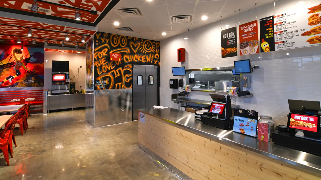 Interior mural of Dave's Hot Chicken in Champaign, IL, showing vibrant graffiti art, red seating and the service area.