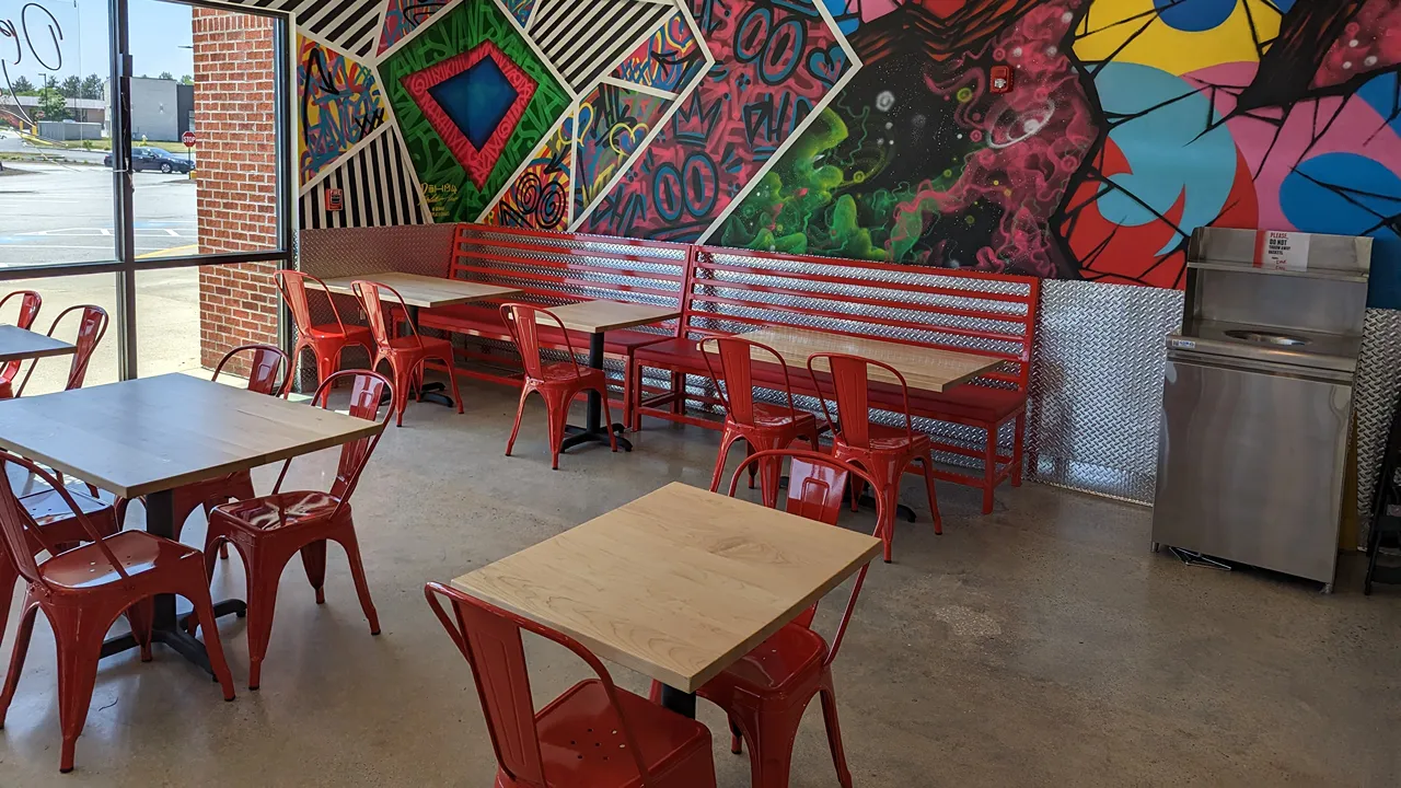 Interior of Dave's Hot Chicken, Chelmsford, MA, showcasing bright red seating, vibrant mural walls. a food station and a view to the outside carpark.