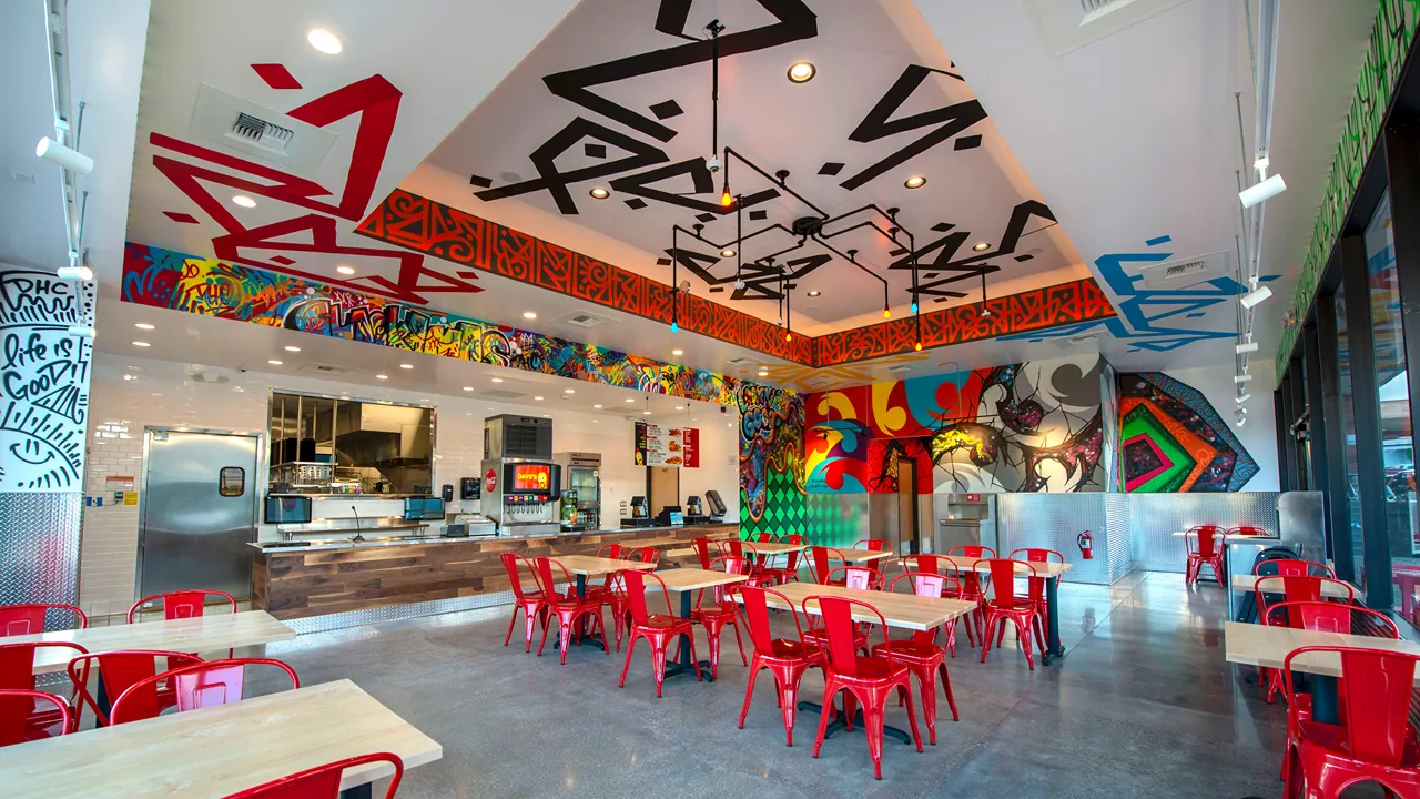 Spacious interior at Dave's Hot Chicken in Clackamas, OR, featuring red chairs, vibrant ceiling art, and bold murals on the walls.