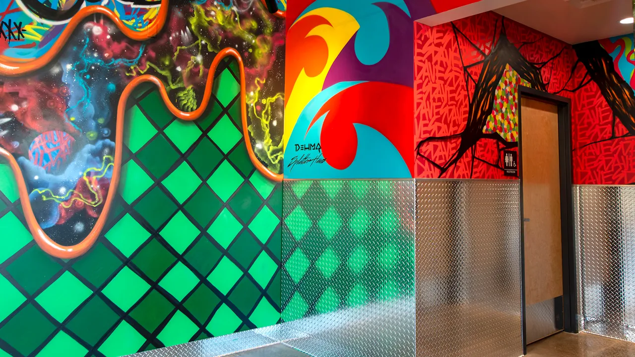 A hallway with bold, colorful murals featuring green and red designs, along with silver metal plating on the lower half of the walls inside Dave's in Clackamas, OR.