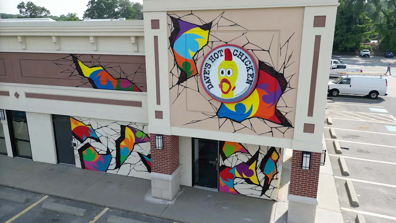 Front exterior of Dave’s Hot Chicken on Cochituate Rd in Framingham, MA, featuring bright signage and colourful artistic wall murals.