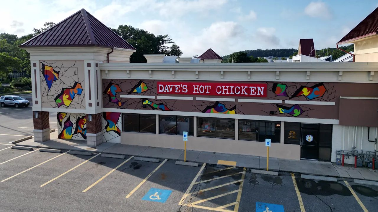 View of Dave’s Hot Chicken on Cochituate Rd in Framingham, MA, showcasing colorful murals and bold restaurant signage.