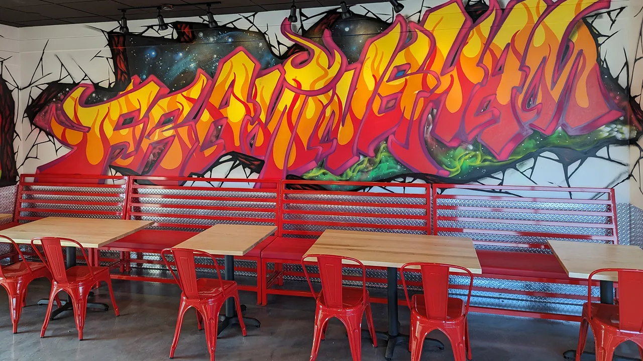 Interior view showing red seating and vibrant graffiti-style murals inside Dave’s Hot Chicken restaurant in Framingham, MA.