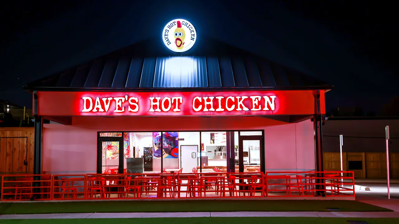 Night view of Dave’s Hot Chicken storefront with bright red signage lit up in Fort Worth, TX on Cockrell Ave.