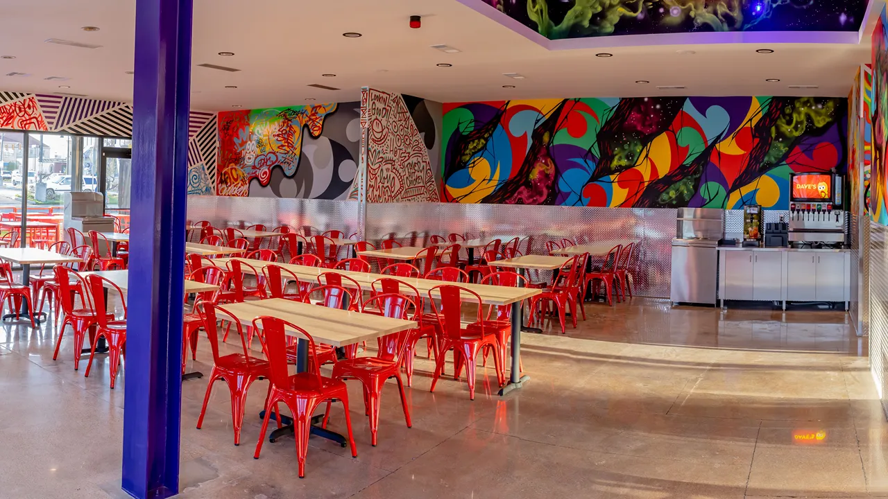 Spacious dining area with red chairs and colorful wall murals at Dave’s Hot Chicken in Fort Worth, TX on Cockrell Ave.