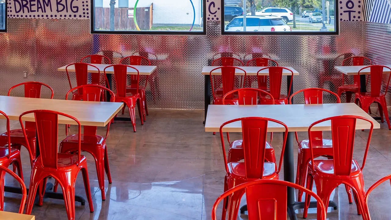 Bright seating area with red chairs and metal walls inside Dave’s Hot Chicken in Fort Worth, TX on Cockrell Ave.