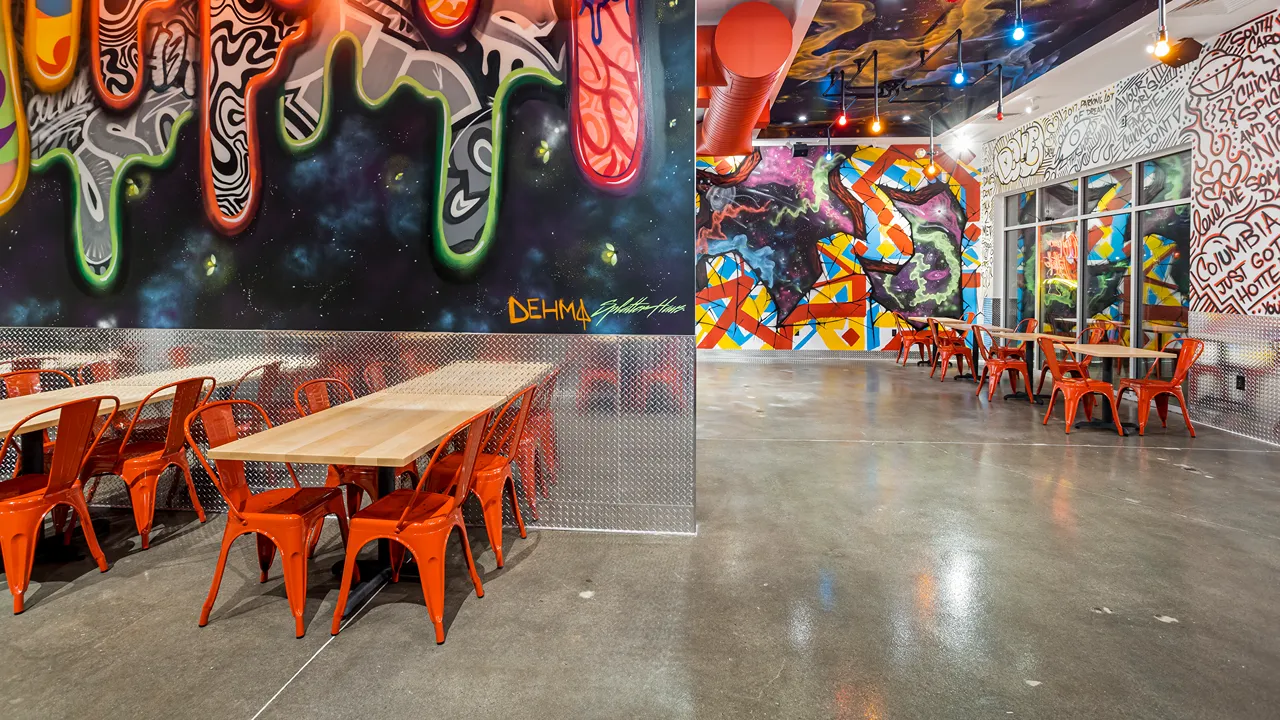 Red chairs and wooden tables with vibrant wall murals inside a Dave's Hot Chicken in Columbia, SC.