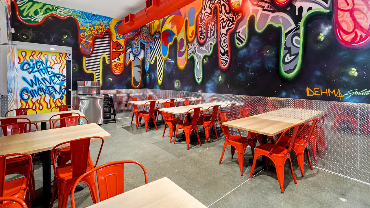 Seating area with colorful murals and red chairs inside Dave's Hot Chicken, Columbia, SC.