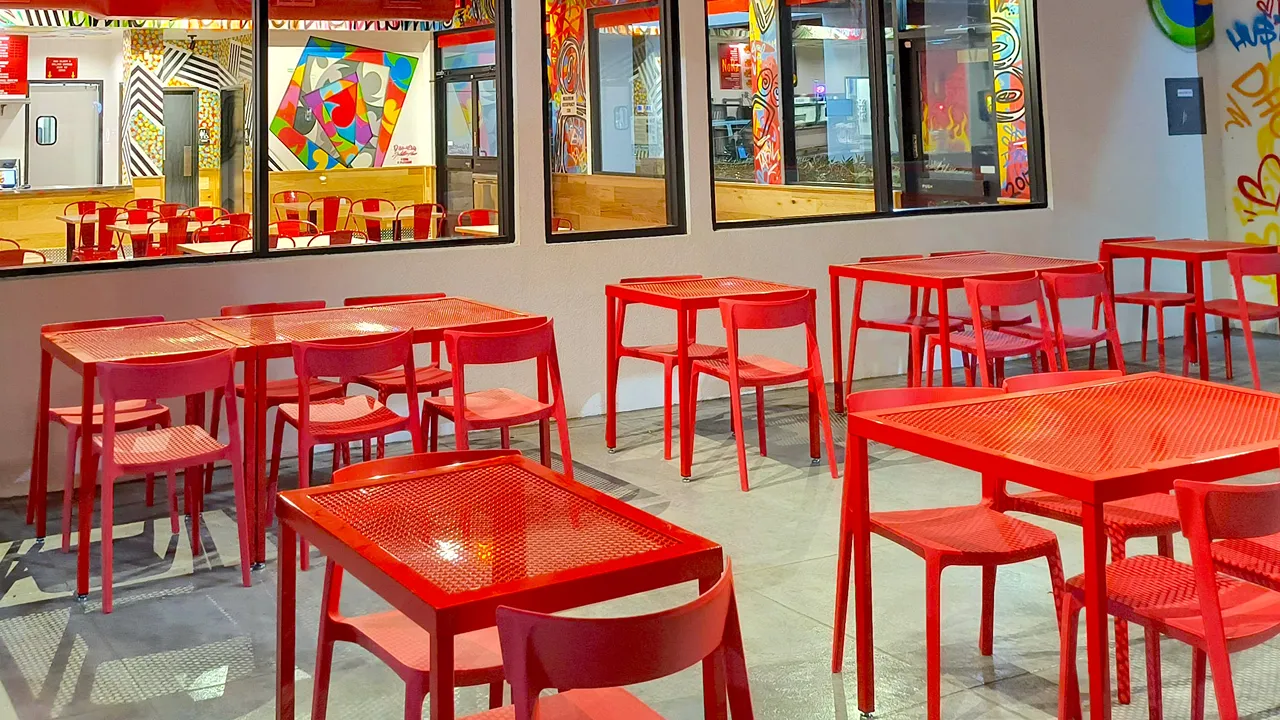 Bright interior with red tables and chairs, colorful murals, and a view into the kitchen at Dave’s Hot Chicken in Gilbert, AZ.