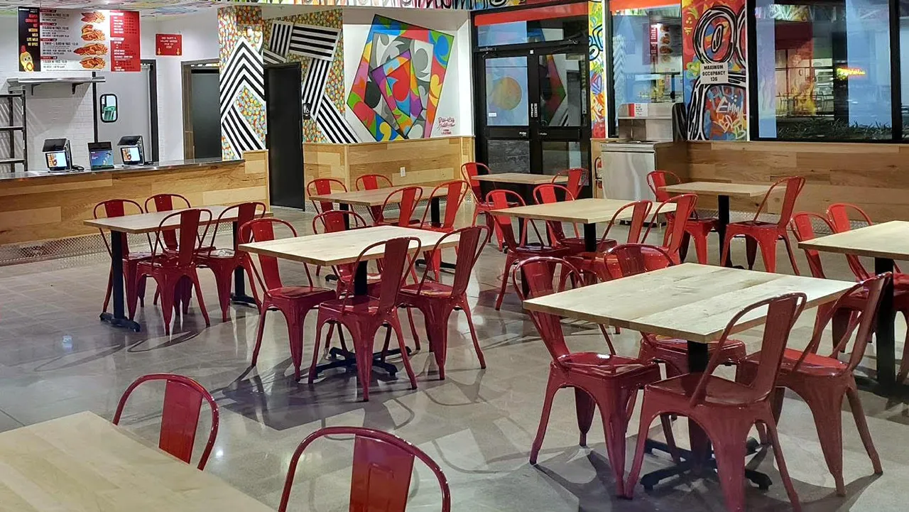 Indoor dining area with red metal chairs and wood tables, surrounded by graffiti-style art on the walls at Dave’s Hot Chicken in Gilbert, AZ.