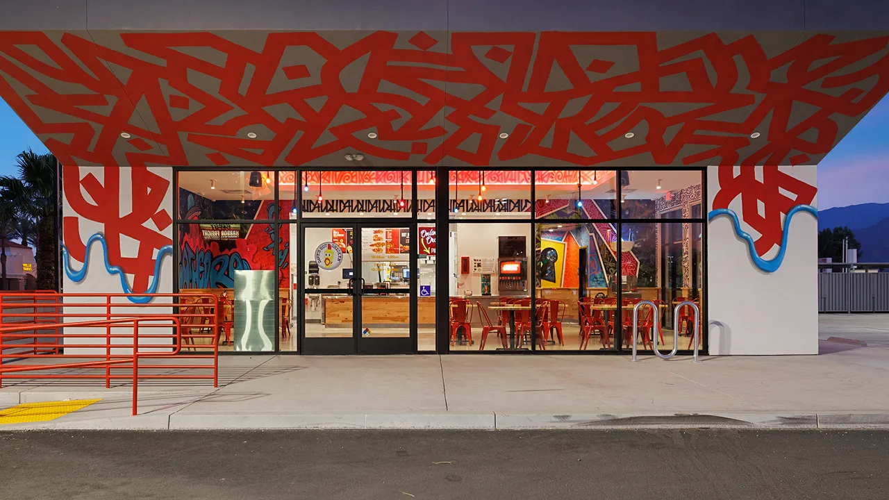 Exterior of Dave's Hot Chicken on Date Palm Drive, Cathedral City, CA, featuring vibrant graffiti art and modern glass storefront.