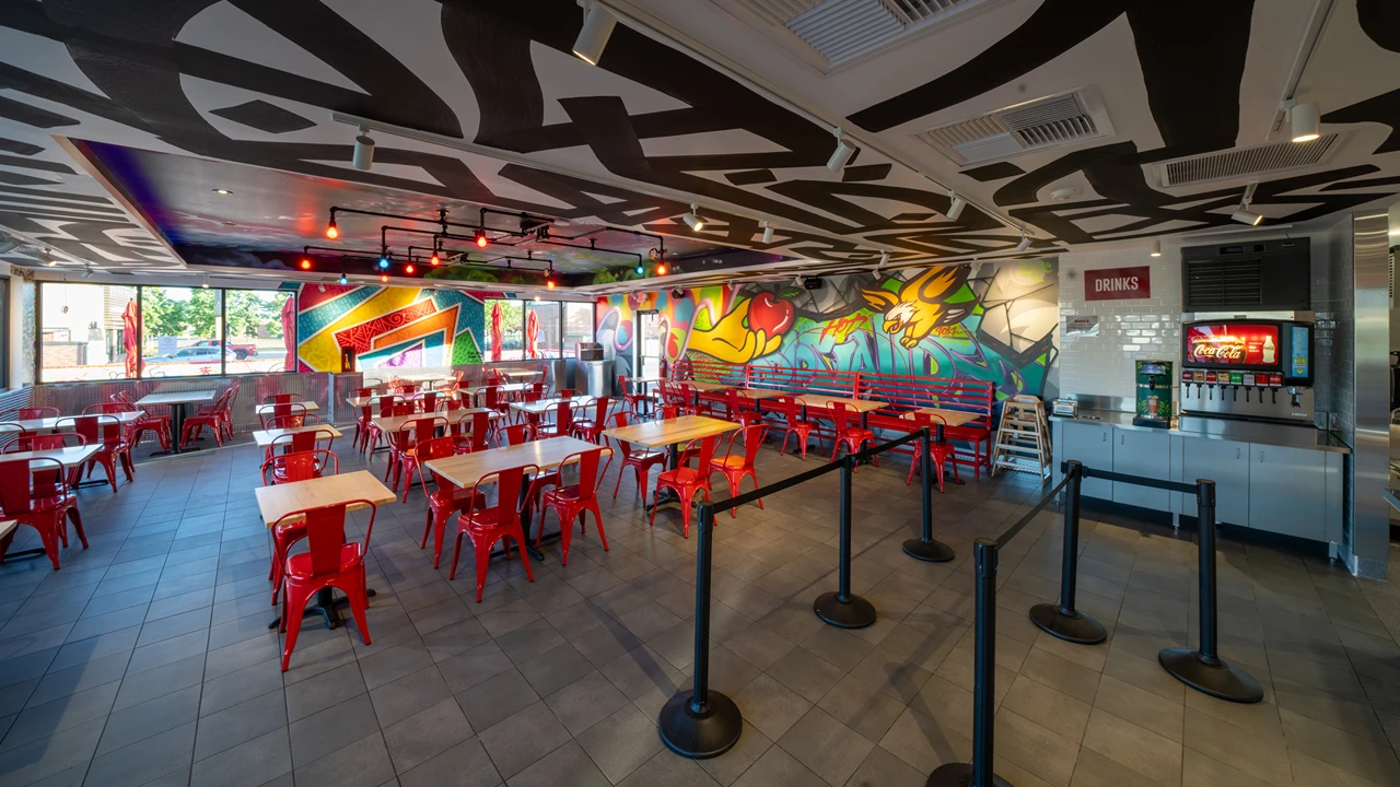 Spacious dining area inside Dave's Hot Chicken in Apple Valley, MN, featuring colorful murals and red seating.