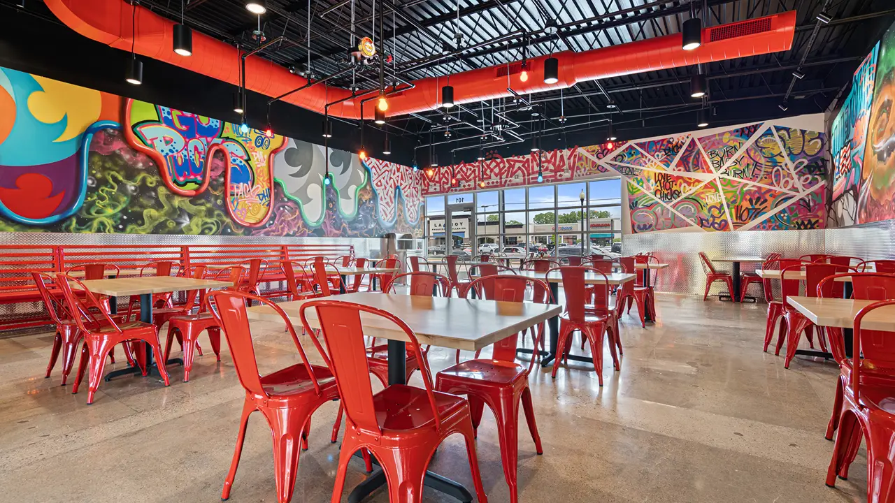 Colorful dining area inside Dave's Hot Chicken in Ashwaubenon, WI, near Green Bay, with red seating and vibrant murals.