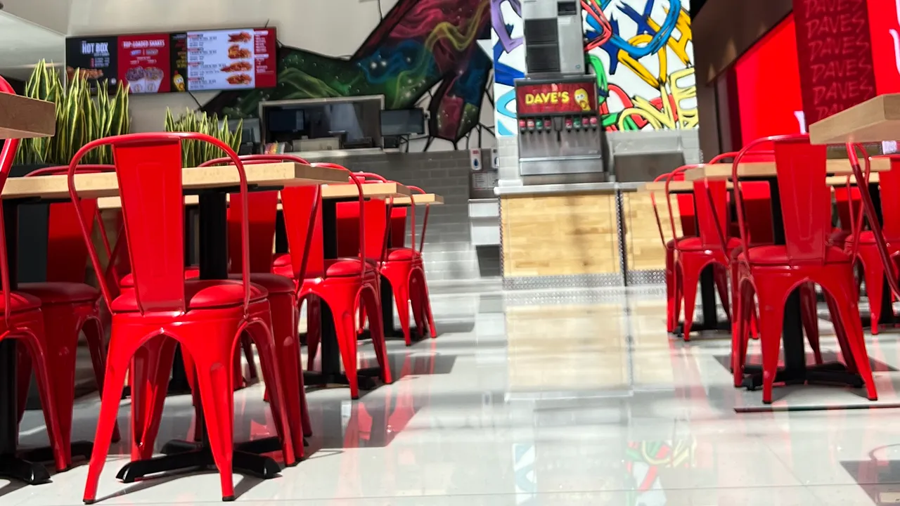 Red chairs and tables in front of a counter with vibrant murals inside Dave's Hot Chicken, Dubai Mall, Dubai.