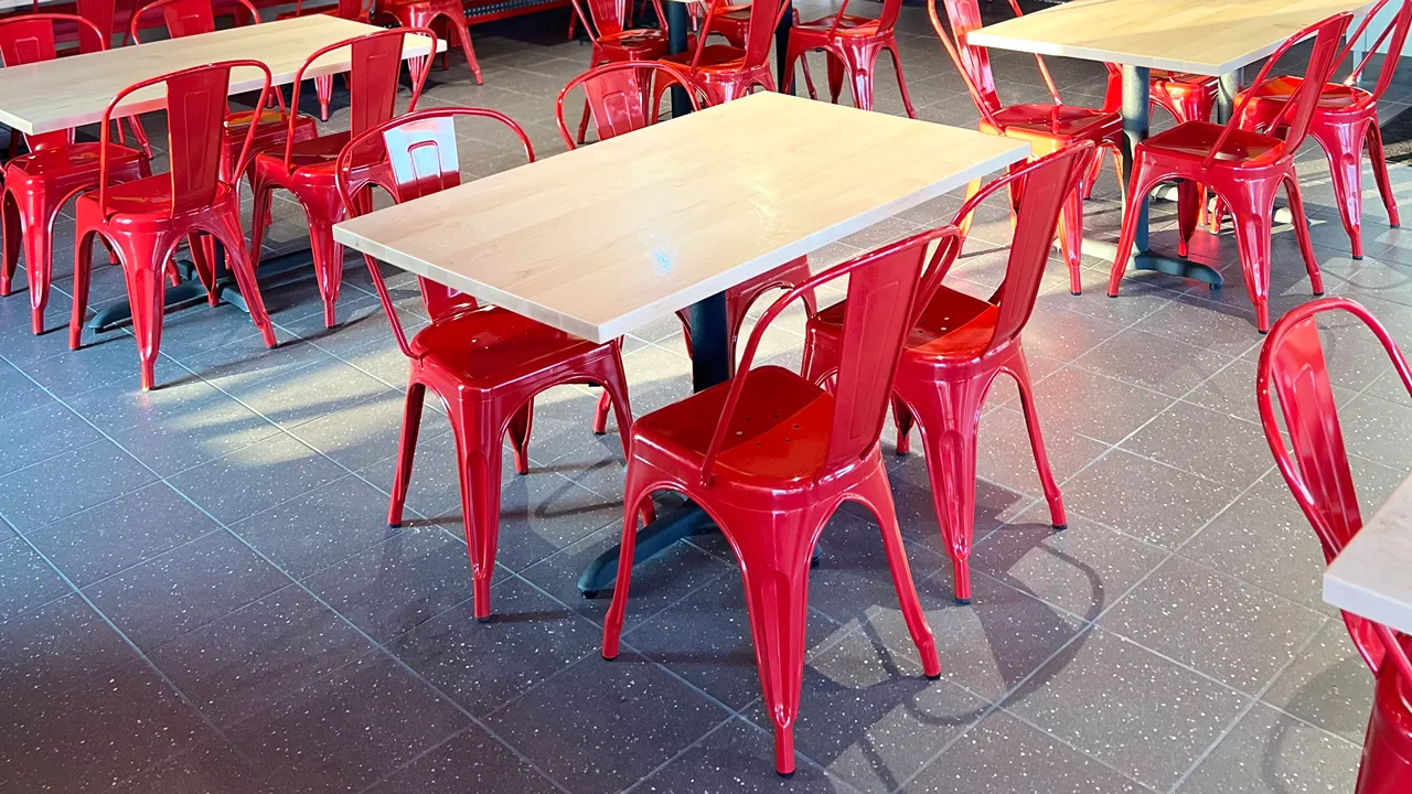 Close-up of red metal chairs and wooden tables in the dining area of Dave's Hot Chicken on E. Fowler Ave, Tampa, FL near USF.