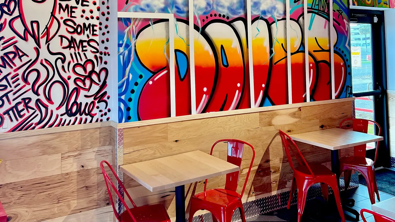 Wall art and vibrant seating arrangement in the dining area of Dave's Hot Chicken on E. Fowler Ave, Tampa, FL near USF.