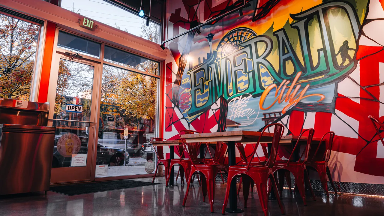 Interior seating area with red chairs and tables at Dave's Hot Chicken on E. Pike St, Seattle, WA, with Emerald City mural.